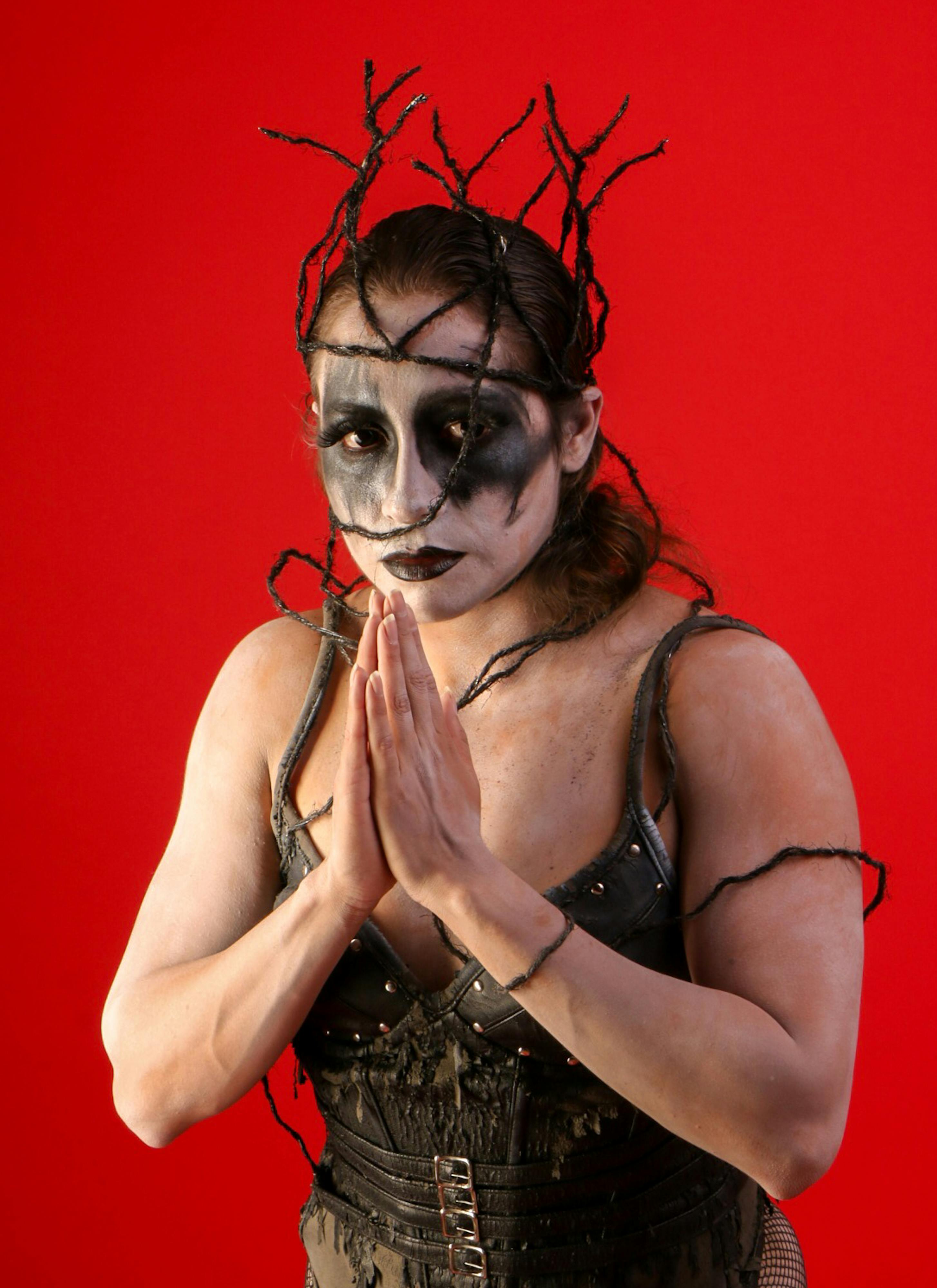 Free Person in theatrical makeup and costume poses with hands in prayer against a vibrant red backdrop. Stock Photo