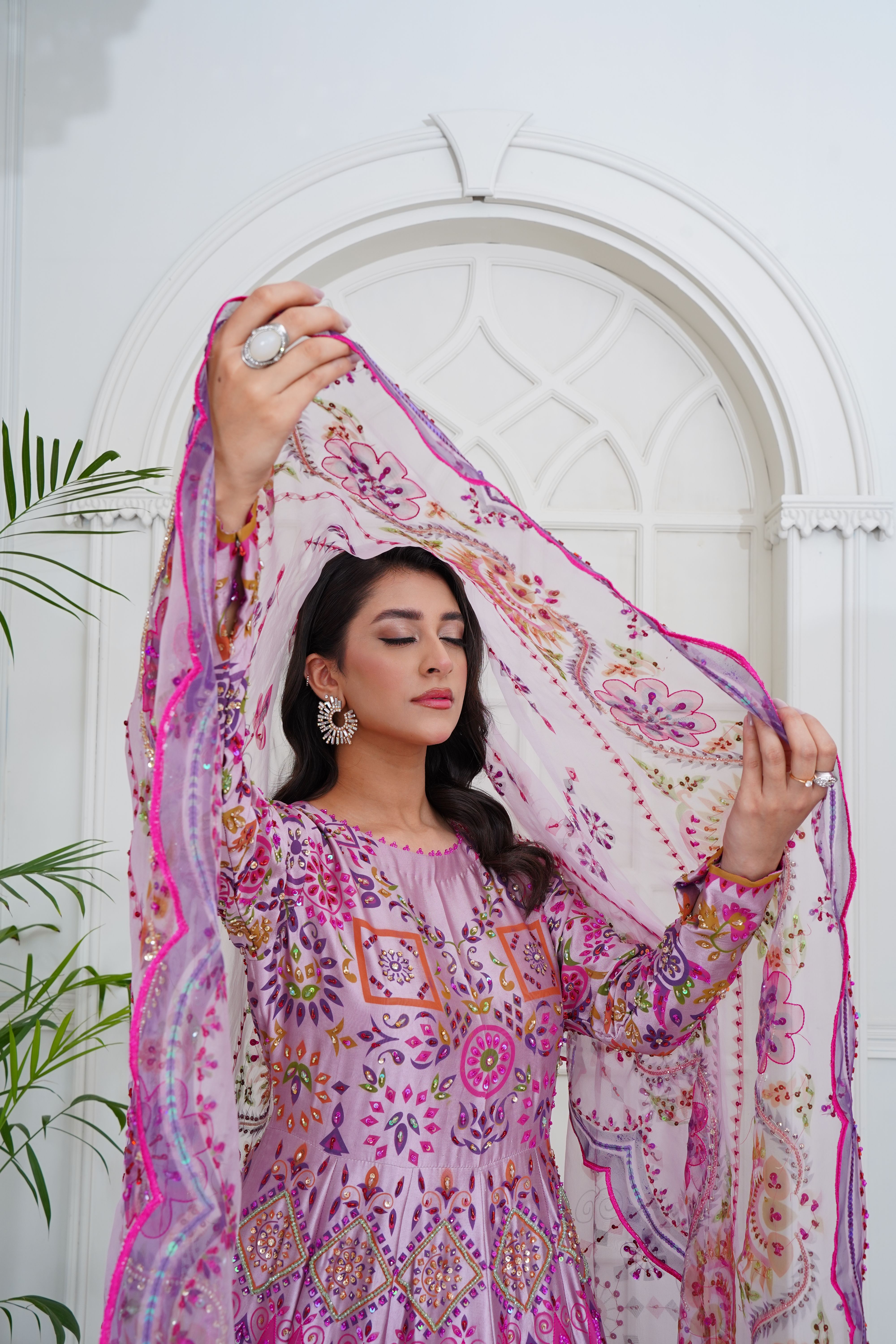 A stunning fashion model poses in a traditional South Asian dress inside a beautifully decorated room.