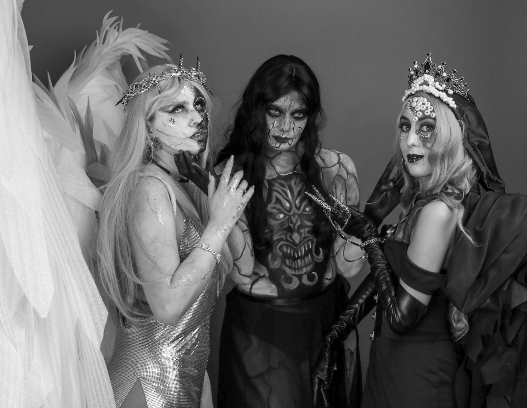 Three people in elaborate fantasy costumes with Halloween makeup in a striking black and white portrait.