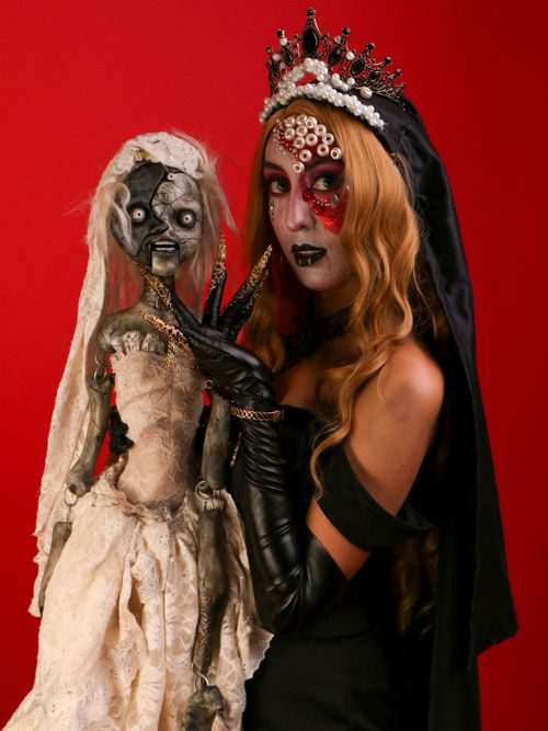 Free A woman in gothic makeup holds a creepy doll against a vivid red background. Stock Photo