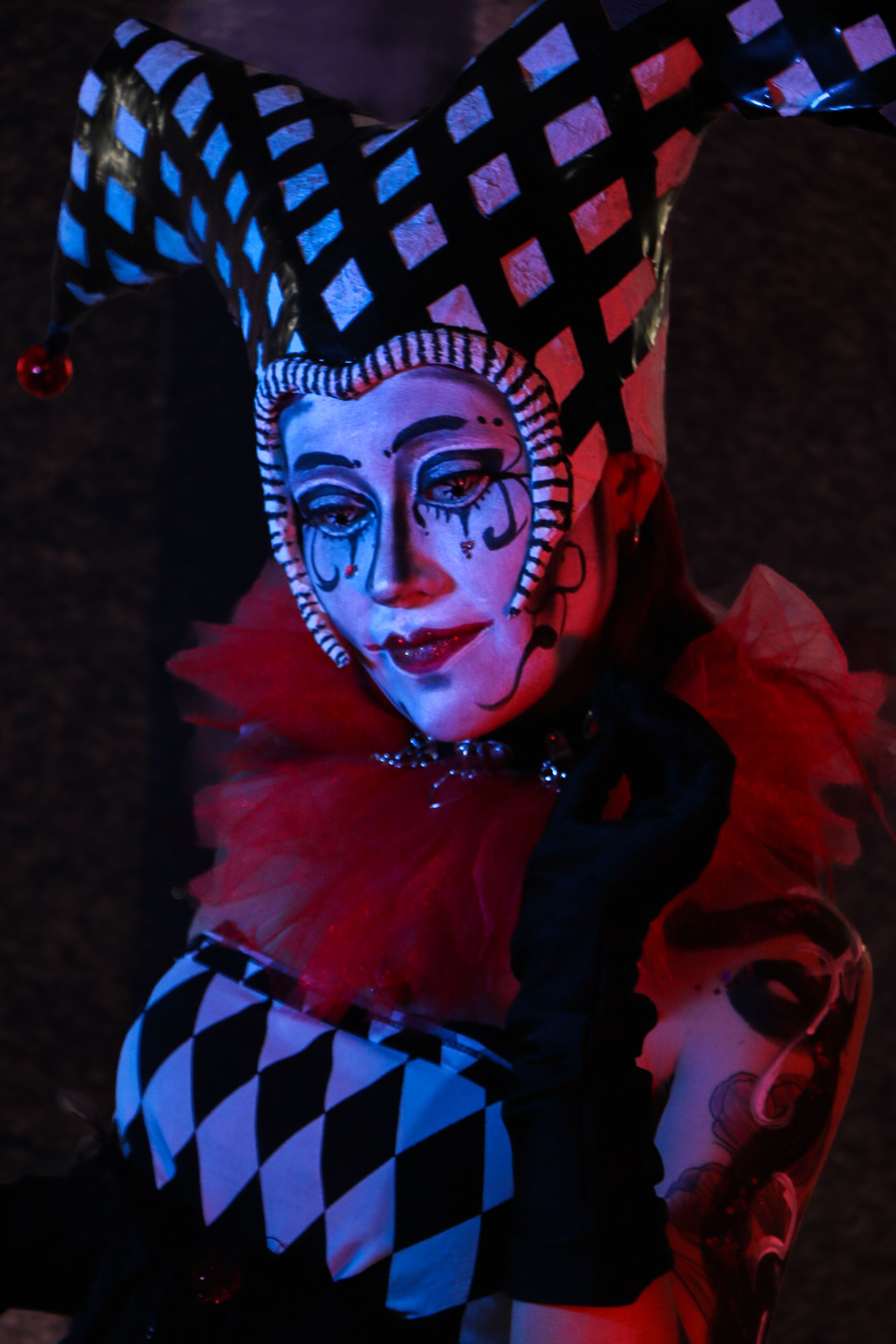 A dramatic carnival jester dressed in a classic harlequin costume, posing with theatrical makeup.