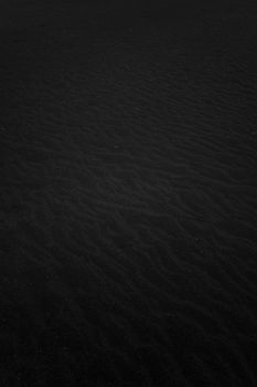 A close-up of a textured black sand surface, capturing its natural patterns in a minimalist style.