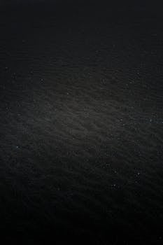 An abstract image featuring a dark textured surface with subtle wave patterns and specks of light.