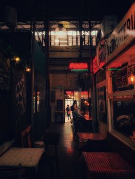 Moody indoor alley view in Buenos Aires market with neon lights and tables.