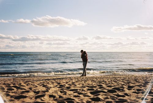 Free A father holding his baby on a peaceful beach under a bright sky, creating a tender moment. Stock Photo