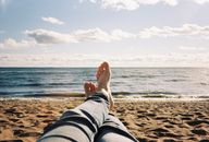 A person relaxing on a sandy beach near the ocean with a clear blue sky.