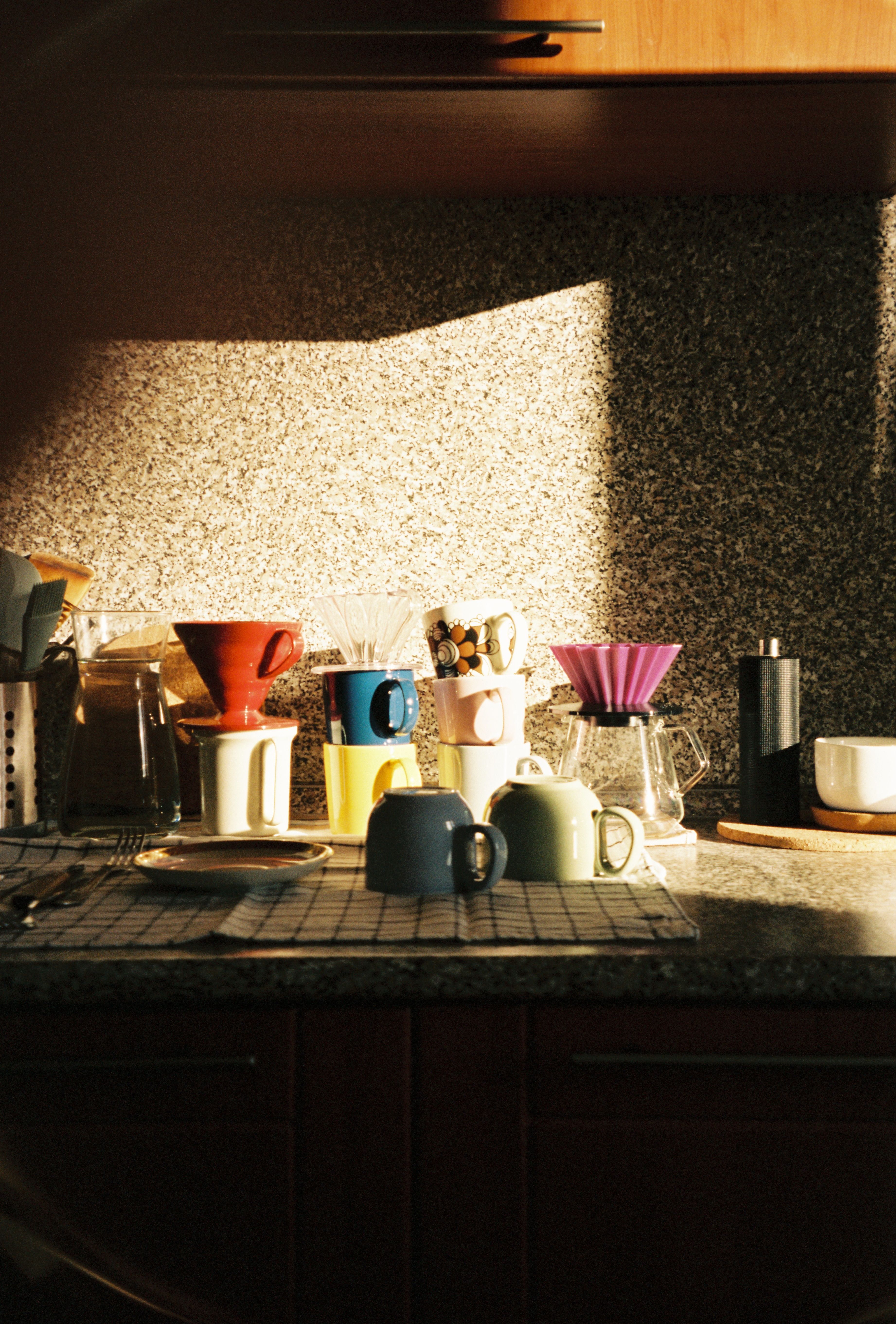 Sunlit kitchen counter arranged with coffee makers, mugs and pour-over equipment