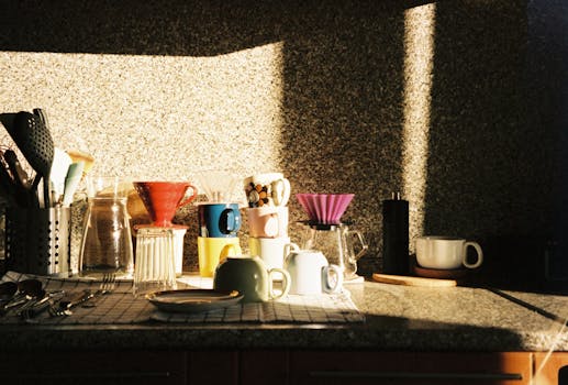 A cozy kitchen counter illuminated by sunlight with various coffee equipment and utensils.