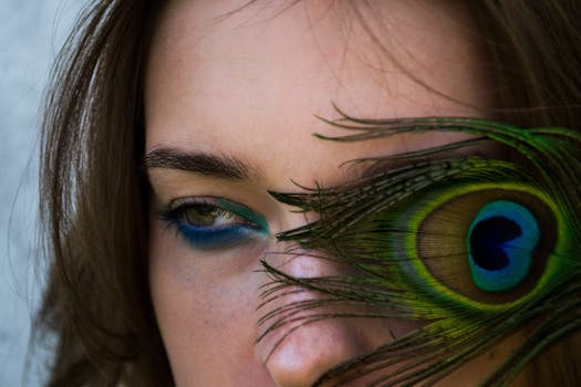 Artistic close-up of a woman's eye with vibrant peacock feather detail, showcasing beauty and glamour.