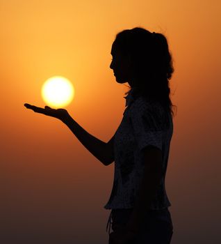 Silhouette of a woman holding the sun against a vivid sunset sky. Captivating and serene.