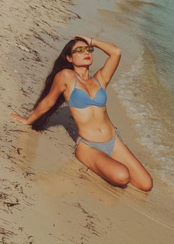 Woman in a blue bikini basking in the sun on a sandy beach.