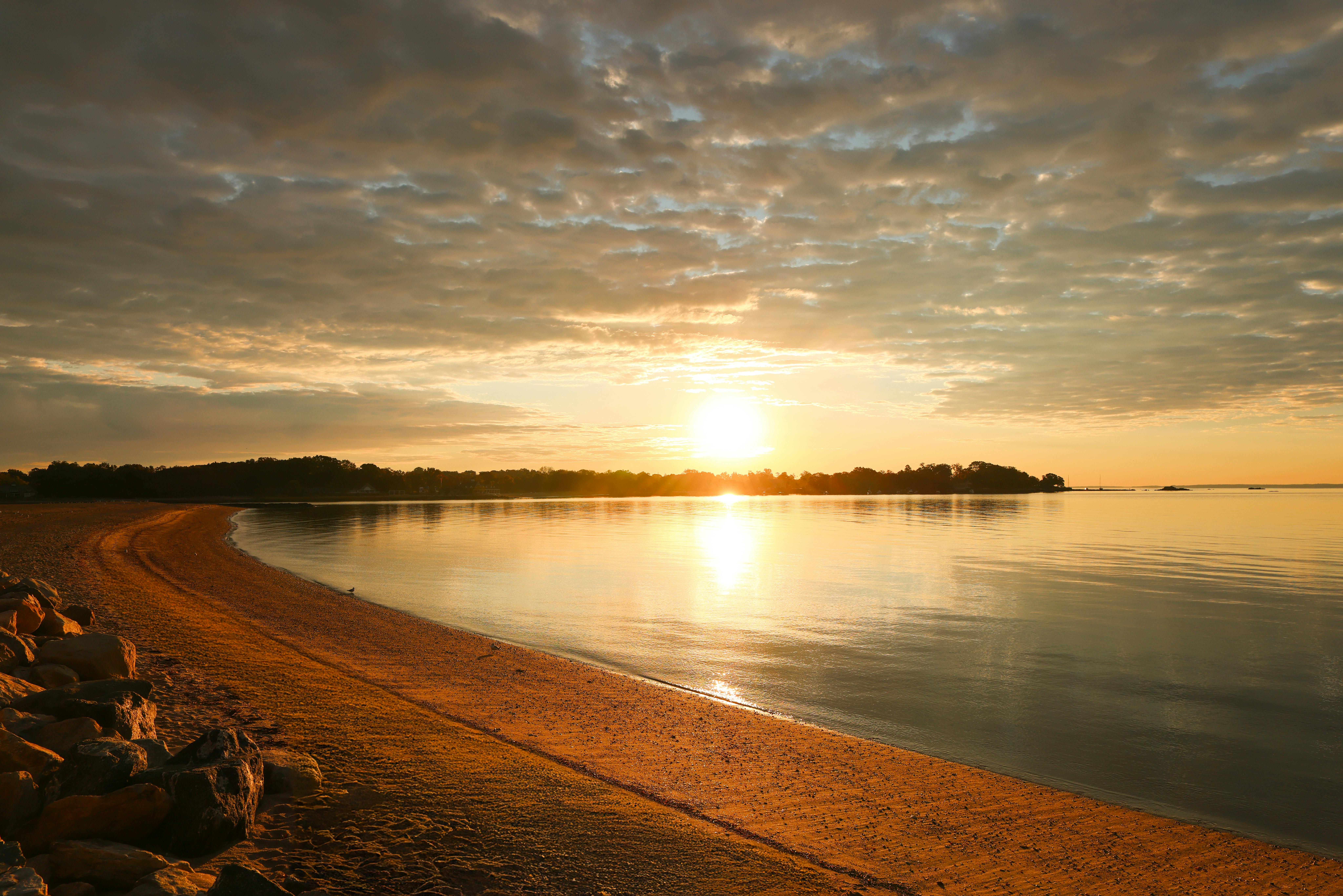 Tranquil sunrise over serene waters and sandy beach at Cove Island Park, Stamford.