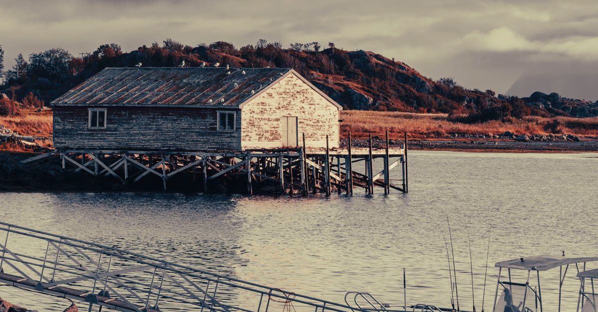 Serene view of a rustic house on stilts by the bay in Norway with anchored boats.