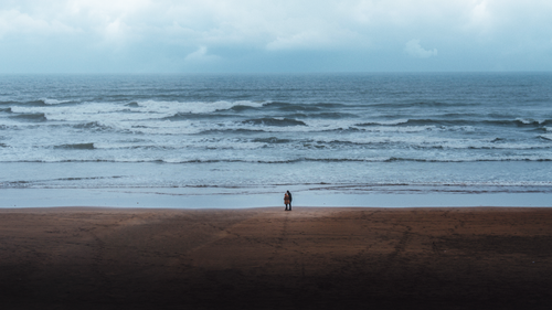 Free Couple enjoying a peaceful walk on a sandy beach with calming ocean waves in the background. Stock Photo