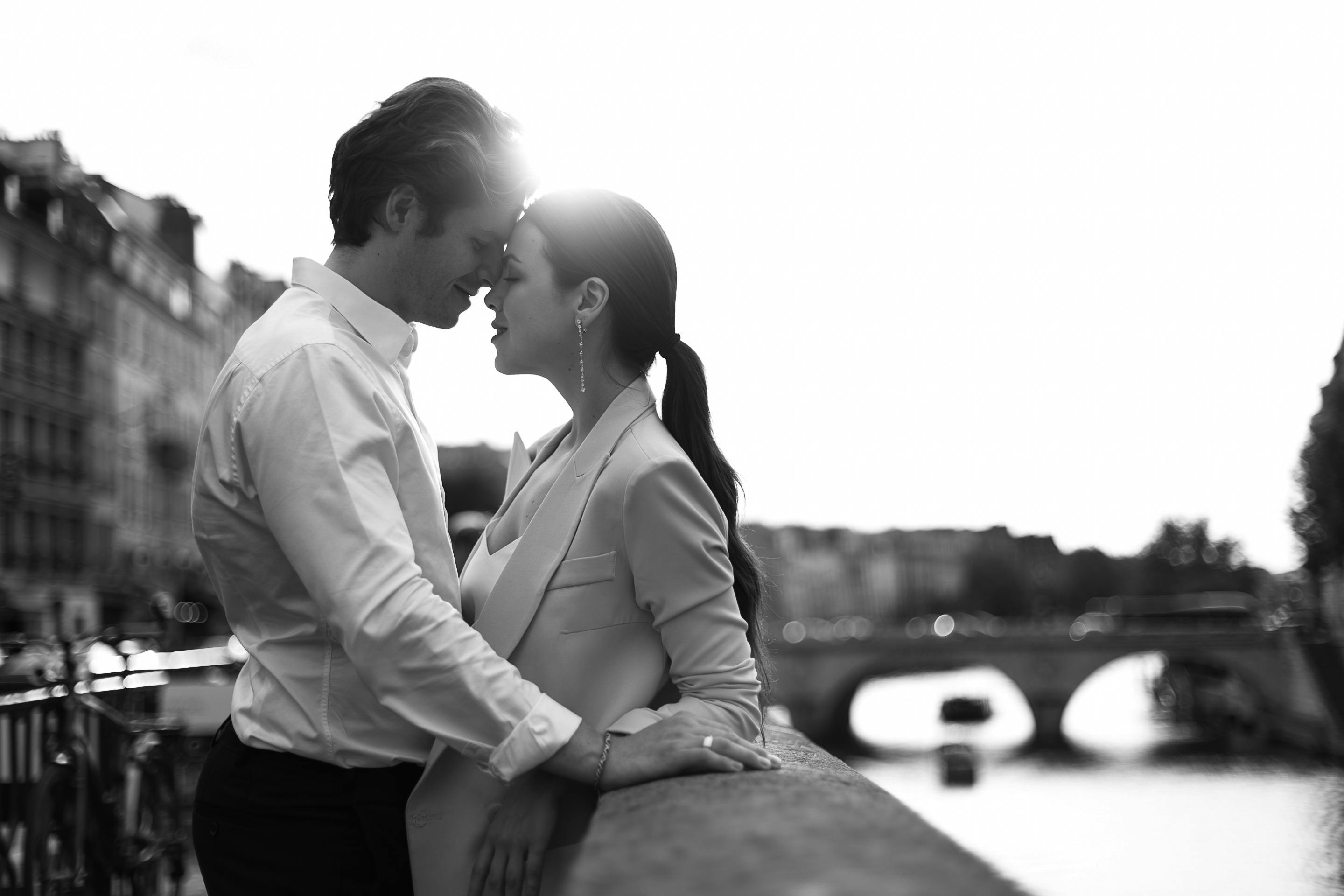 Romantic black and white scene of a couple embracing on a Paris bridge, cityscape backdrop.