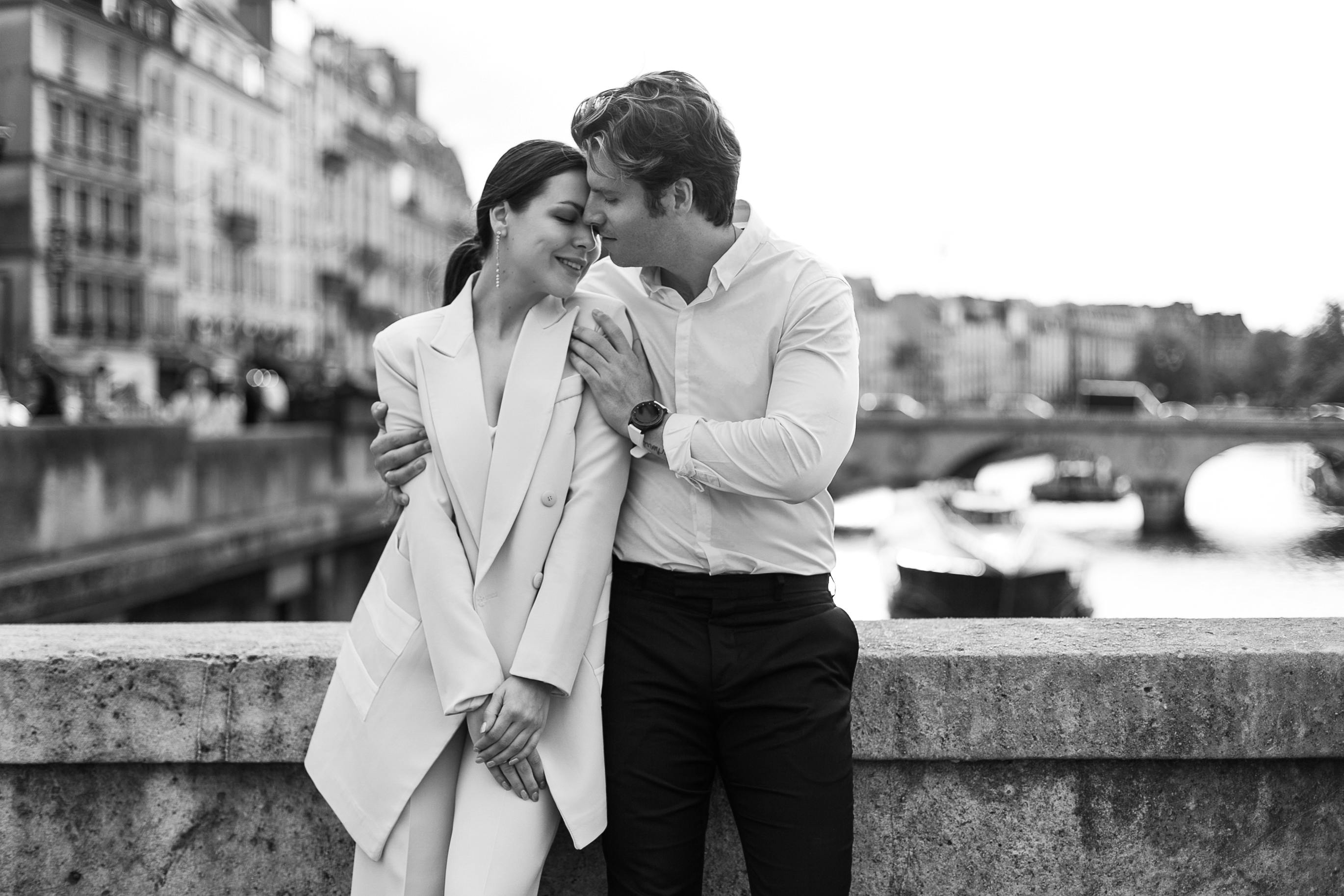 A loving couple shares an intimate moment by the Seine River in Paris, exuding romance.