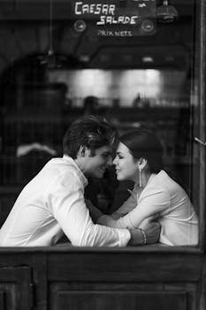 Intimate moment between a couple in a cozy café setting, captured in black and white.
