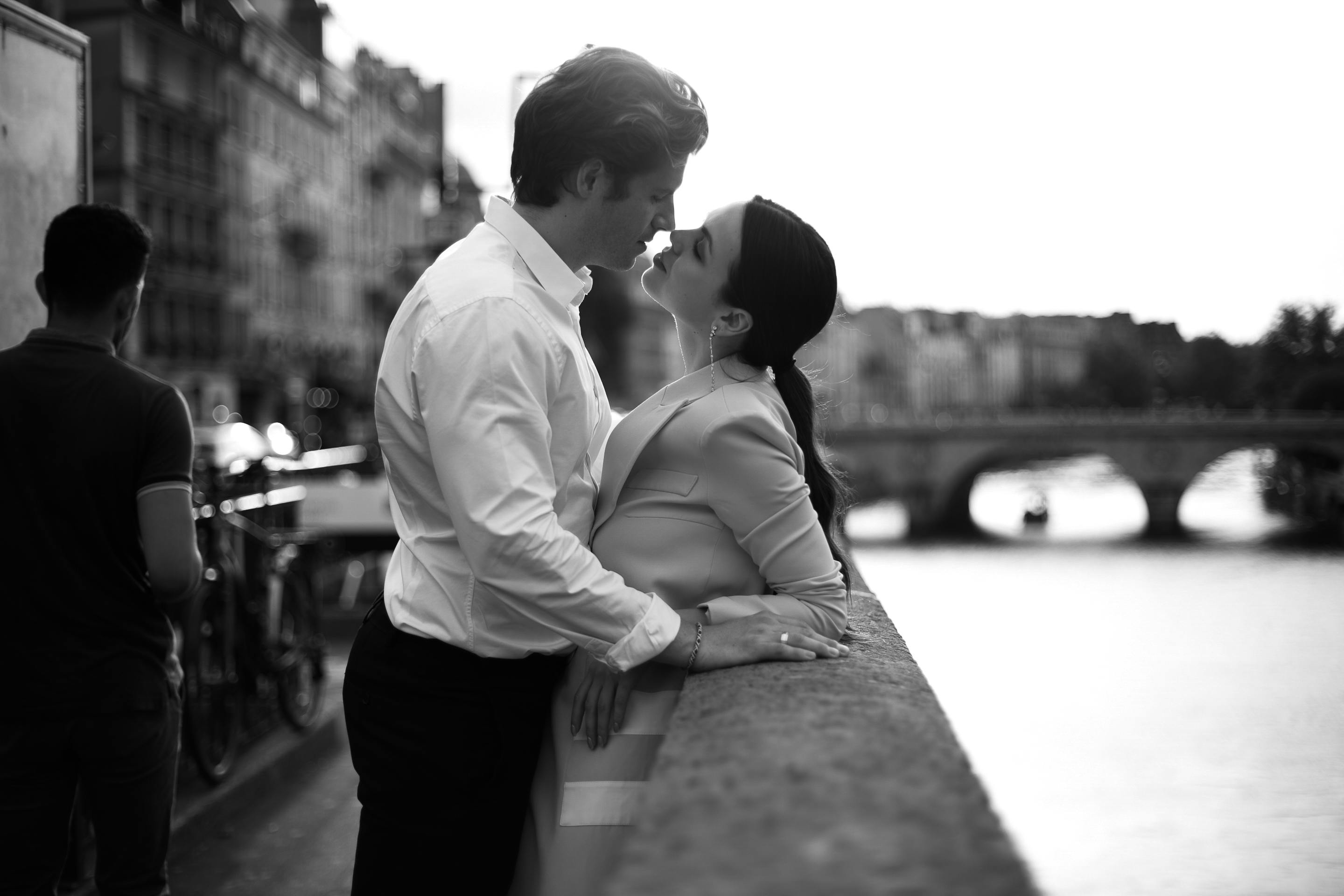 A romantic couple shares a kiss along the Seine River in Paris, encapsulating classic love.