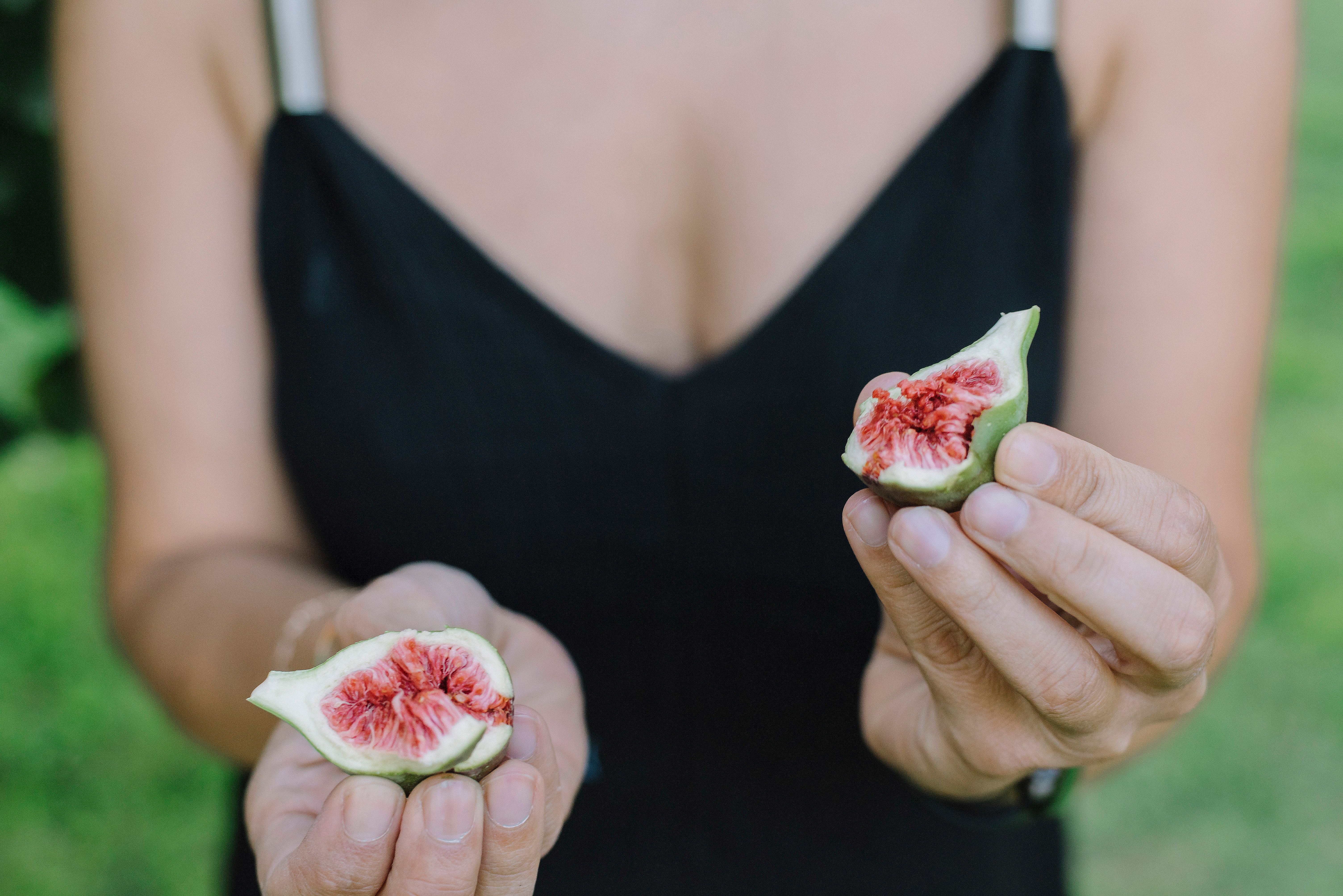 Person holding freshly cut figs outdoors with a blurred green background.