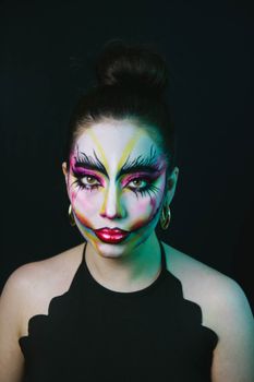 A woman with colorful artistic makeup poses against a dark background.