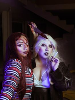 Two women dressed in horror-themed costumes, one holding a knife.