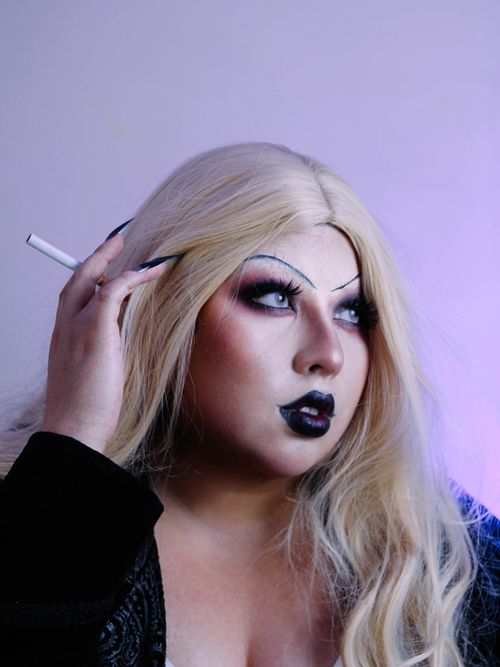 Free A striking portrait of a person with dramatic drag makeup and a blonde wig, holding a cigarette. Stock Photo