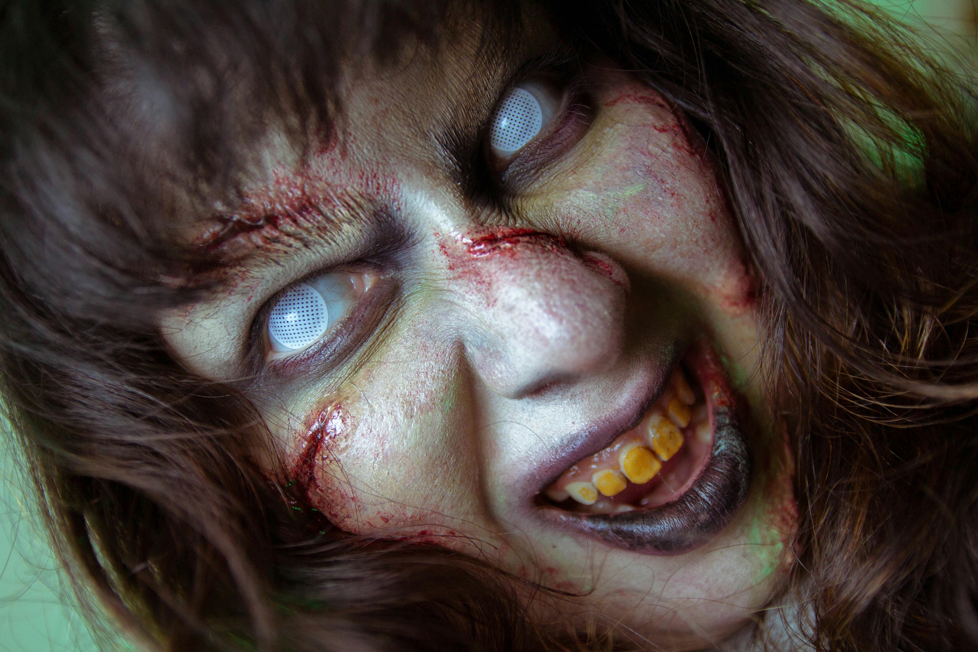 Frightening close-up of a zombie with white eyes and gory makeup, perfect for Halloween themes.