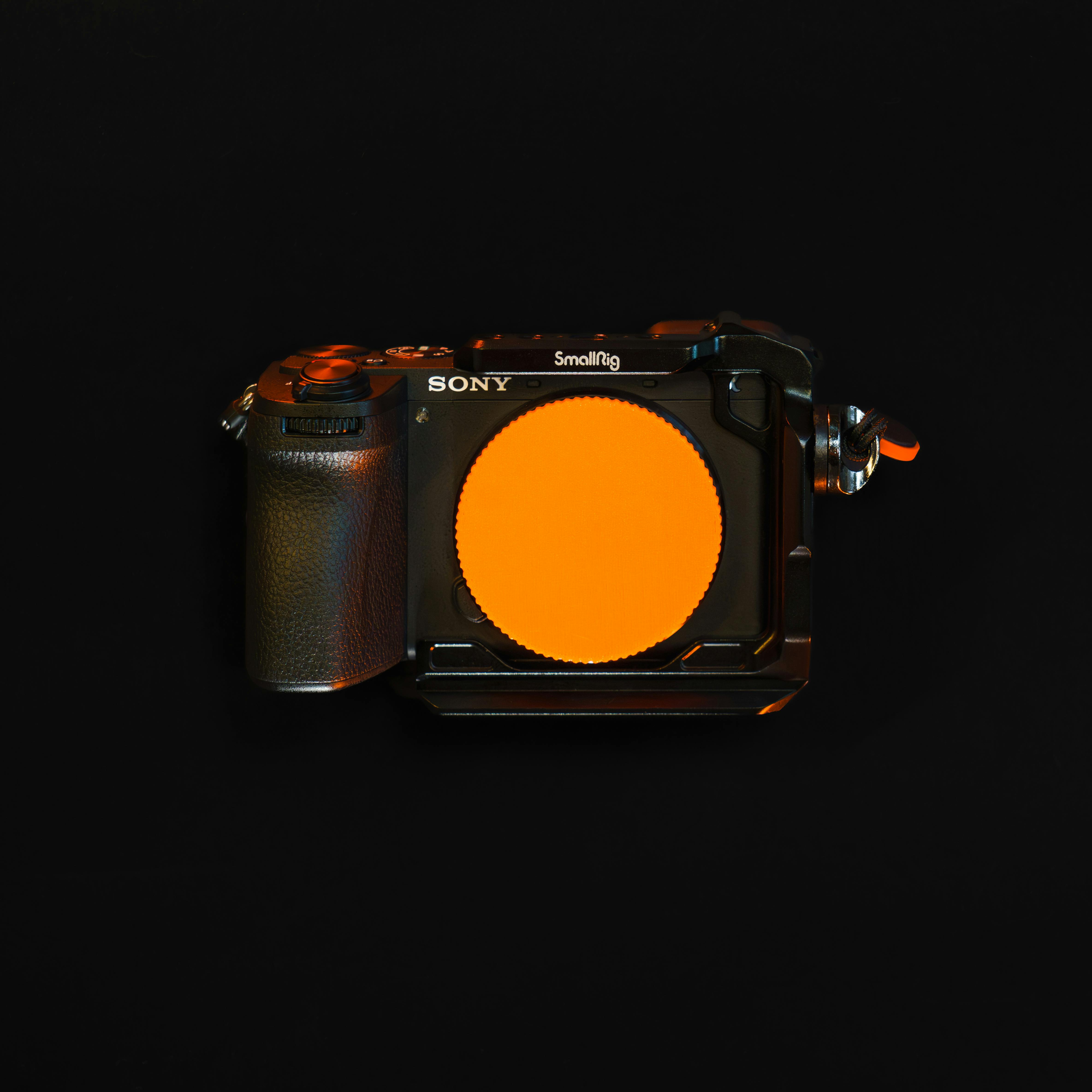 sony camera with orange lens cap on black background