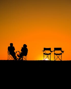 Silhouetted people in chairs against a vivid sunset sky, evoking tranquility and leisure.