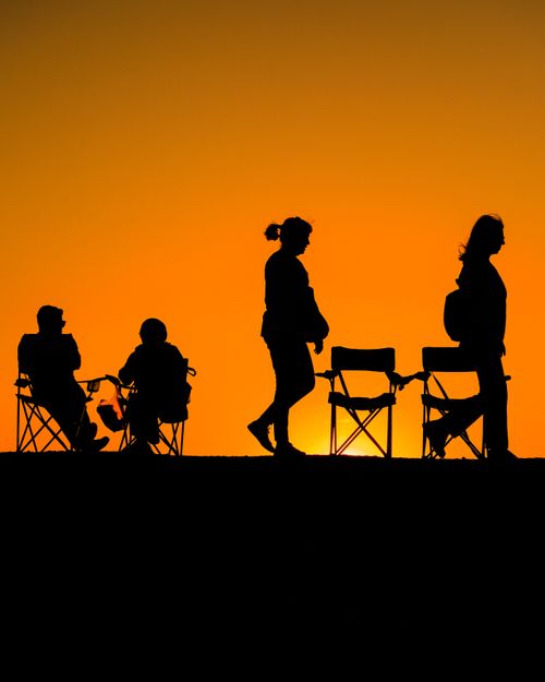 Free Silhouetted adults relax in chairs against a vibrant sunset backdrop. Stock Photo