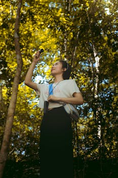 A young woman explores a lush, sunlit forest with a camera, capturing nature's beauty around her.