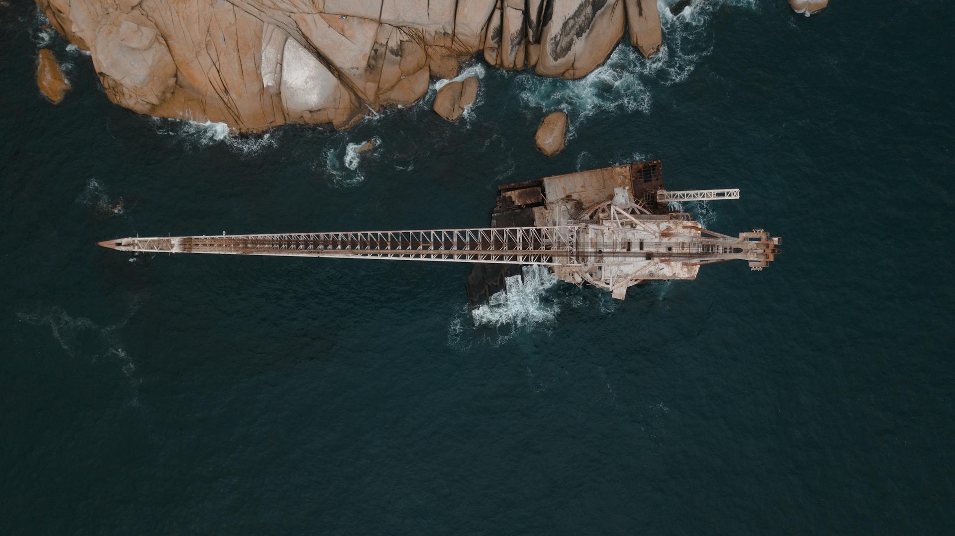 Aerial view of an abandoned rusty platform over a rocky coast and deep ocean.