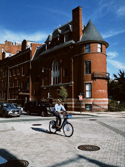 Free A person cycles in an urban setting past a red brick historic building. Stock Photo