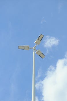 Minimalist view of solar street lamp against a bright blue sky with scattered clouds.