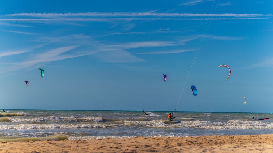 A vibrant scene of kite surfers enjoying a sunny day at the beach with colorful kites in the sky.