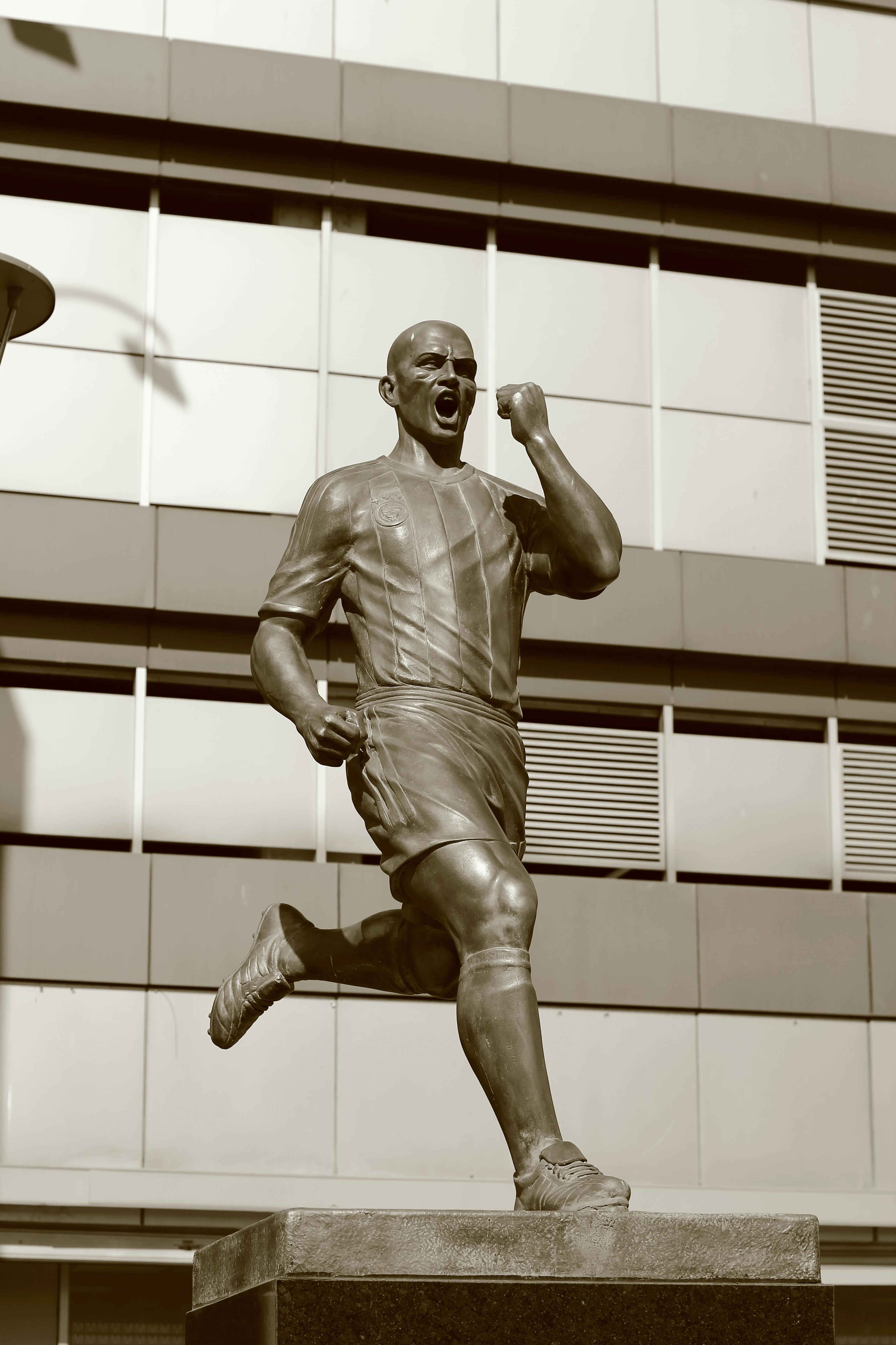 bronze soccer player statue outside modern building