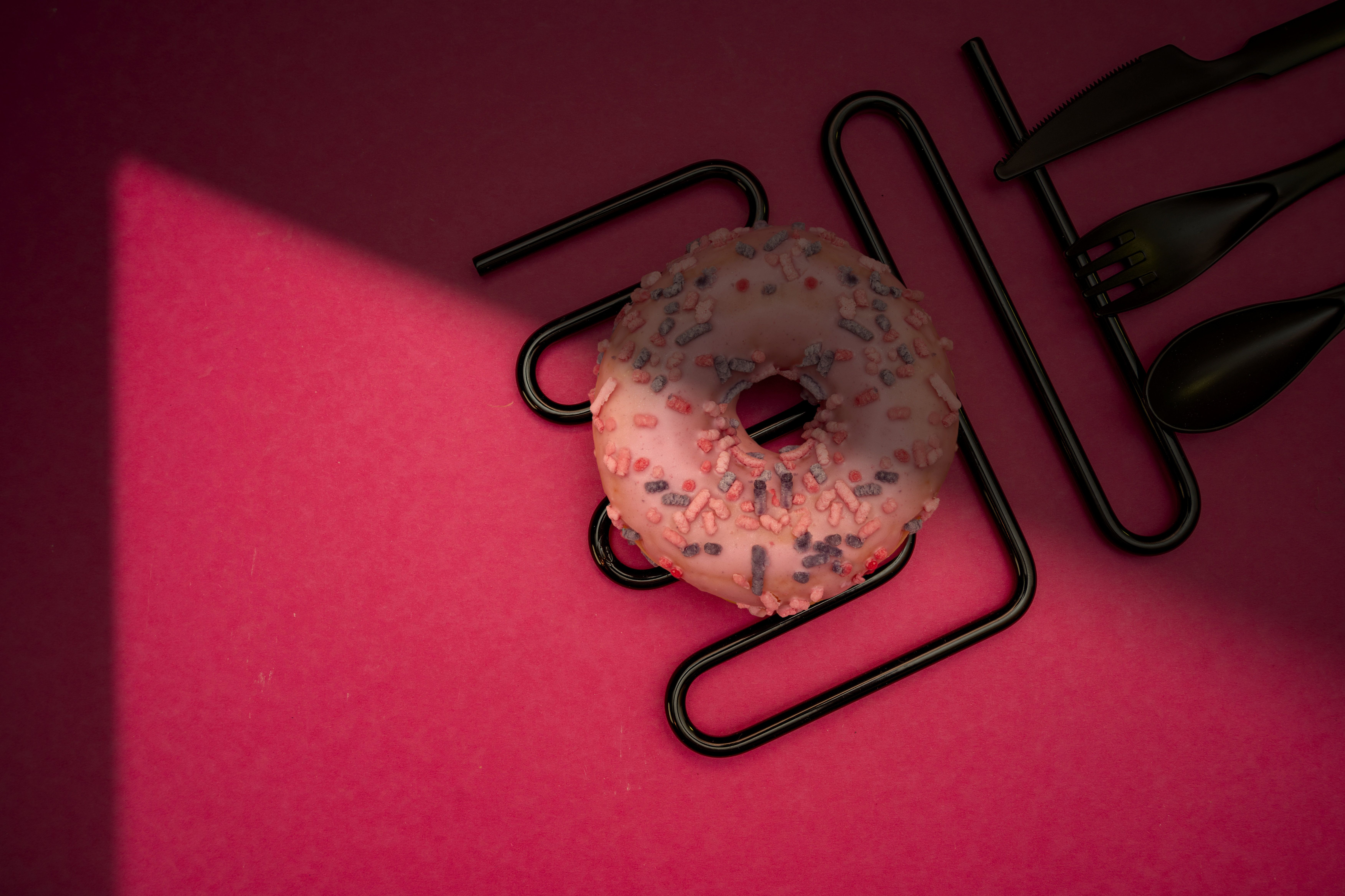 Delicious pink frosted donut with colorful sprinkles on a vibrant pink background, creating a playful and tasty composition.
