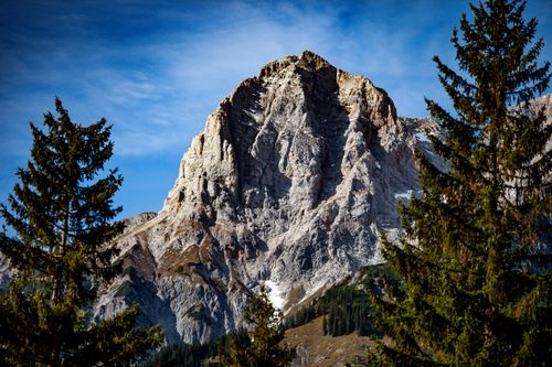 Free A majestic rocky mountain peak framed by evergreen trees under a clear blue sky. Stock Photo