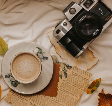 Cozy vintage flat lay featuring a camera, coffee, and autumn leaves for a nostalgic feel.