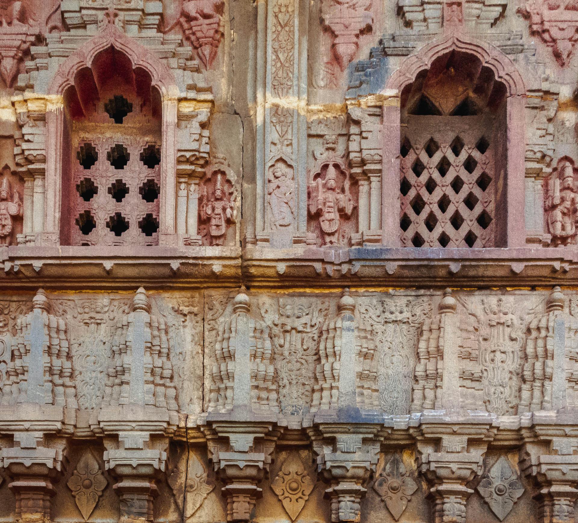 Detailed view of ancient stone carvings and lattice windows on historical Indian building facade.