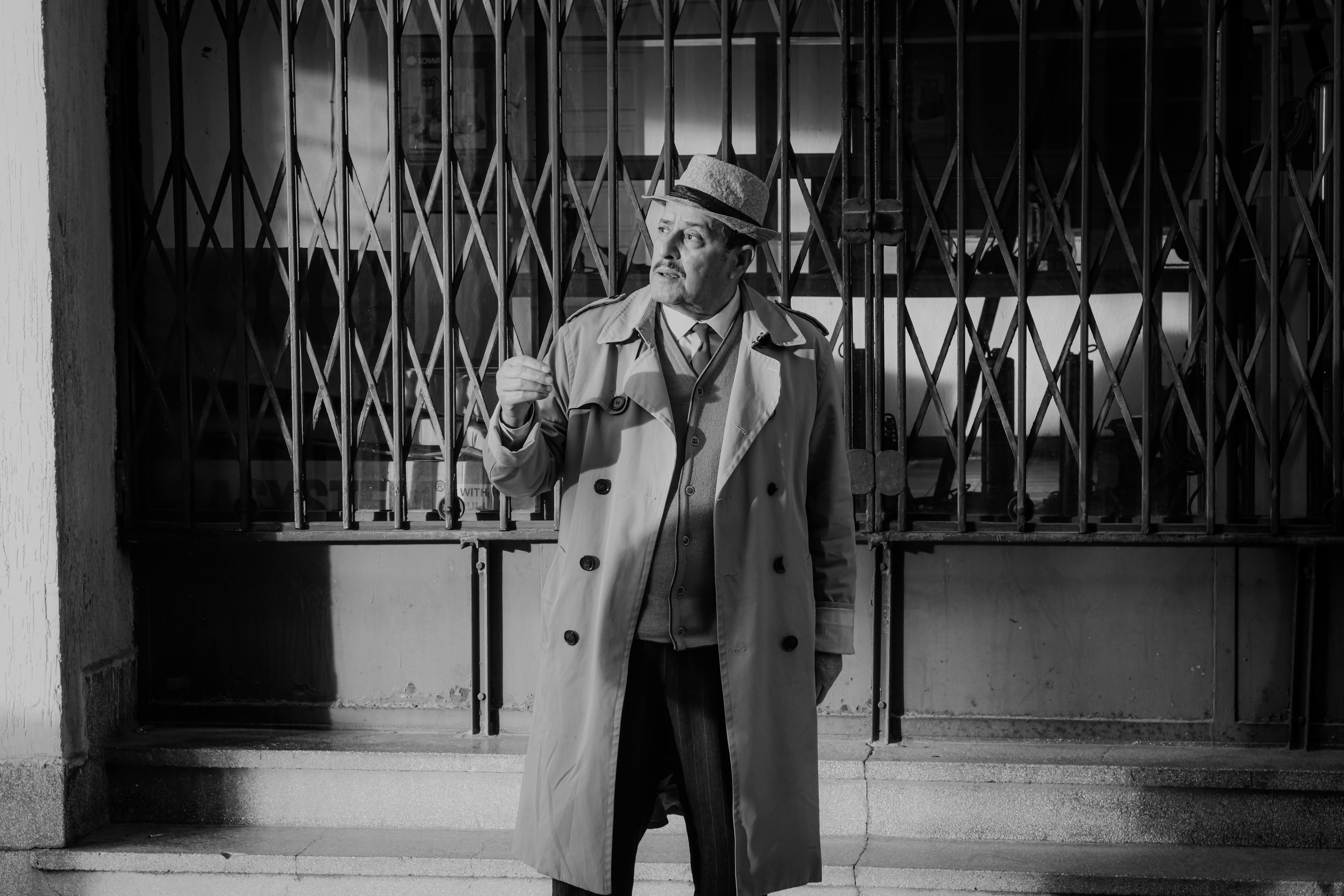 classic noir detective standing outside iron gate