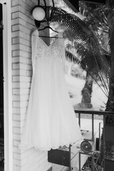 A beautifully detailed white wedding dress hanging outdoors, captured in black and white.