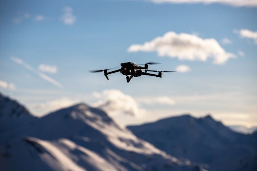 A drone flies over scenic snow-covered peaks under a clear blue sky, capturing breathtaking landscapes.