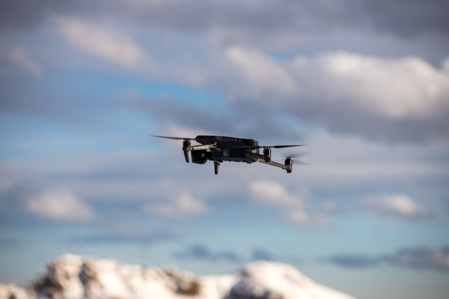 Aerial view of a drone flying over snow-covered mountains with dramatic clouds.