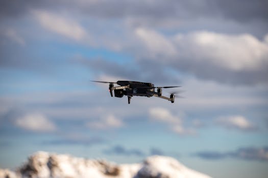 Aerial view of a drone flying over snow-covered mountains with dramatic clouds.