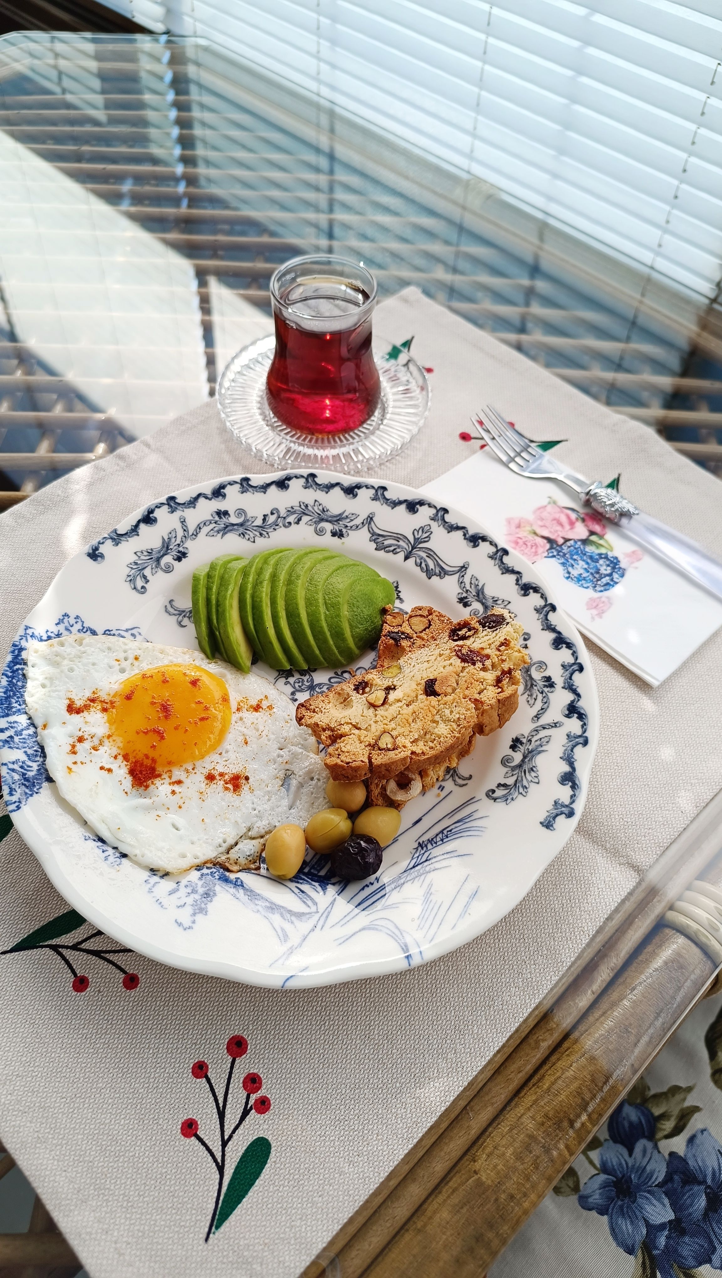 A delicious breakfast featuring fried egg, avocado slices, and tea, styled on a floral plate.
