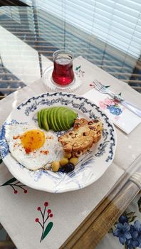A delicious breakfast featuring fried egg, avocado slices, and tea, styled on a floral plate.