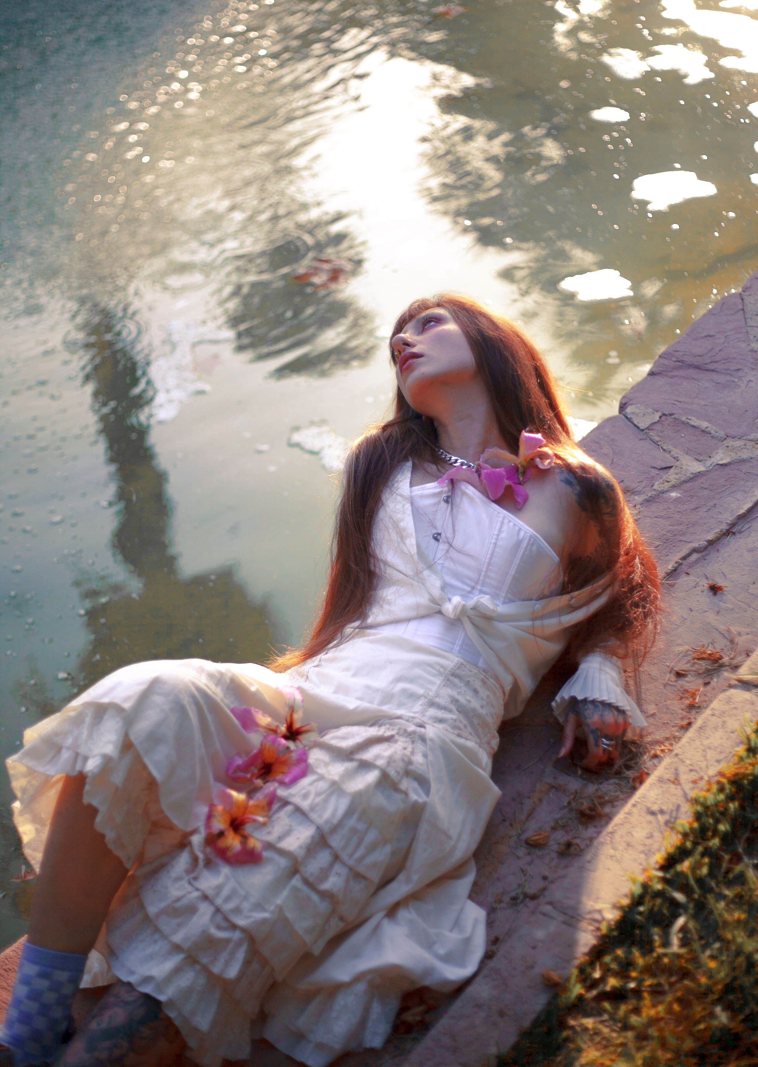 Peaceful woman in white dress by a serene pond with floral accents.