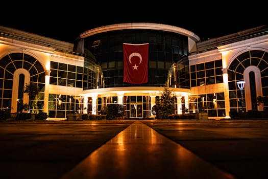 Illuminated modern building with Turkish flag at night, showcasing architecture.