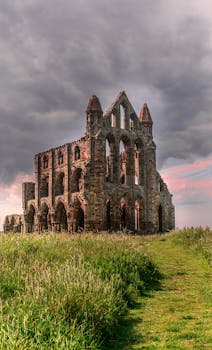 在多云的日落天空下，古老的惠特比修道院哥特式遗址呈现出戏剧性的景观，四周环绕着郁郁葱葱的草地
